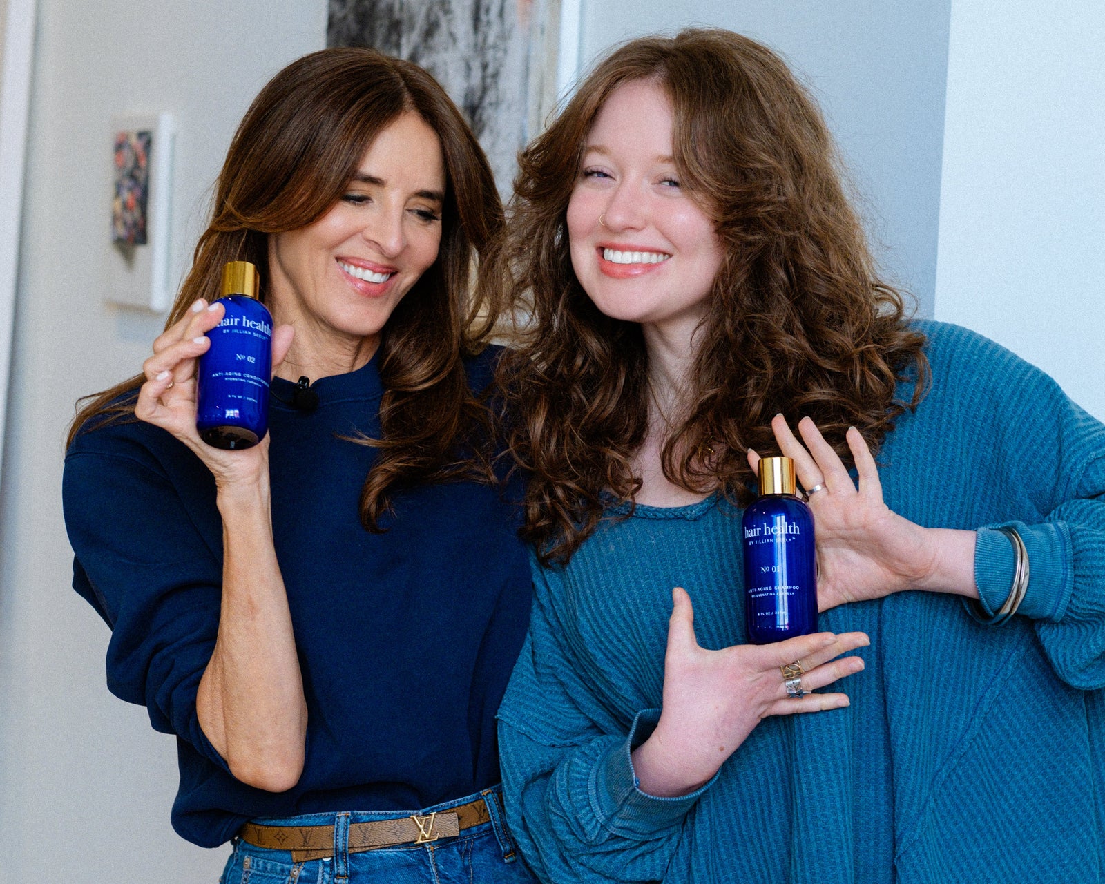 Two women holding blue bottles in a room with a light blue wall.